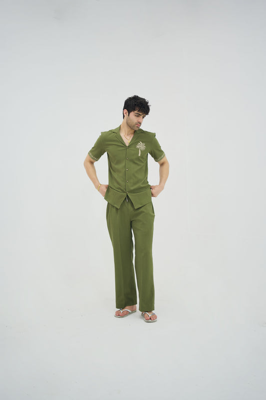 Man posing in a olive green cuban collar shirt and matching tailored trousers by Abbod Atelier on a white studio background.