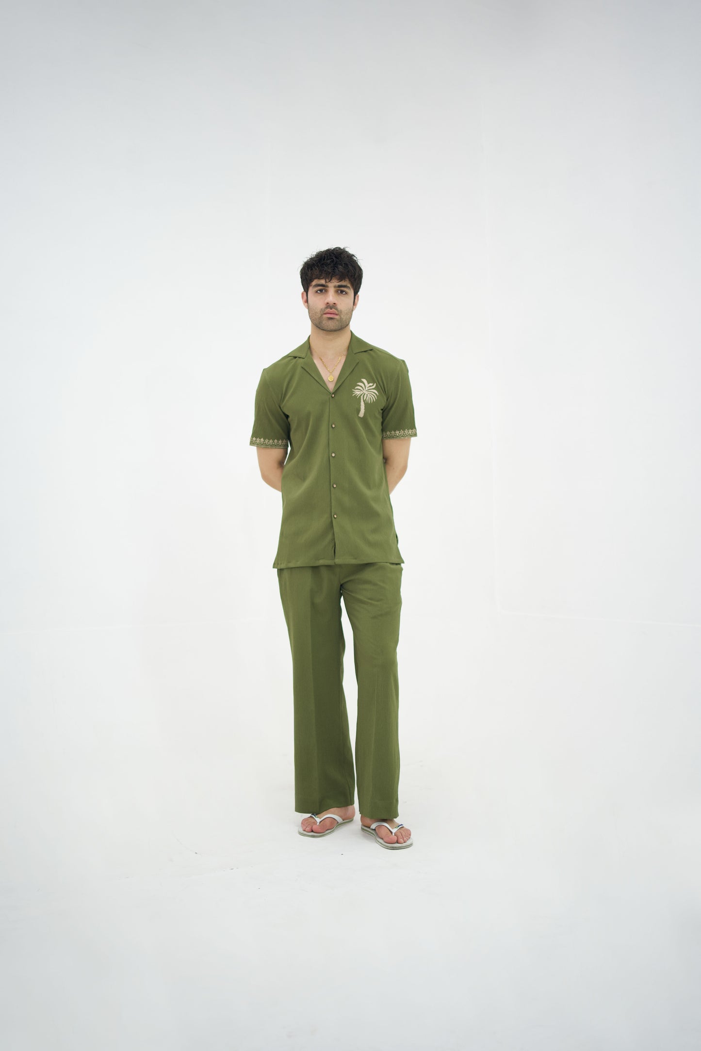 Man posing in a olive green cuban collar shirt and matching tailored trousers by Abbod Atelier on a white studio background.