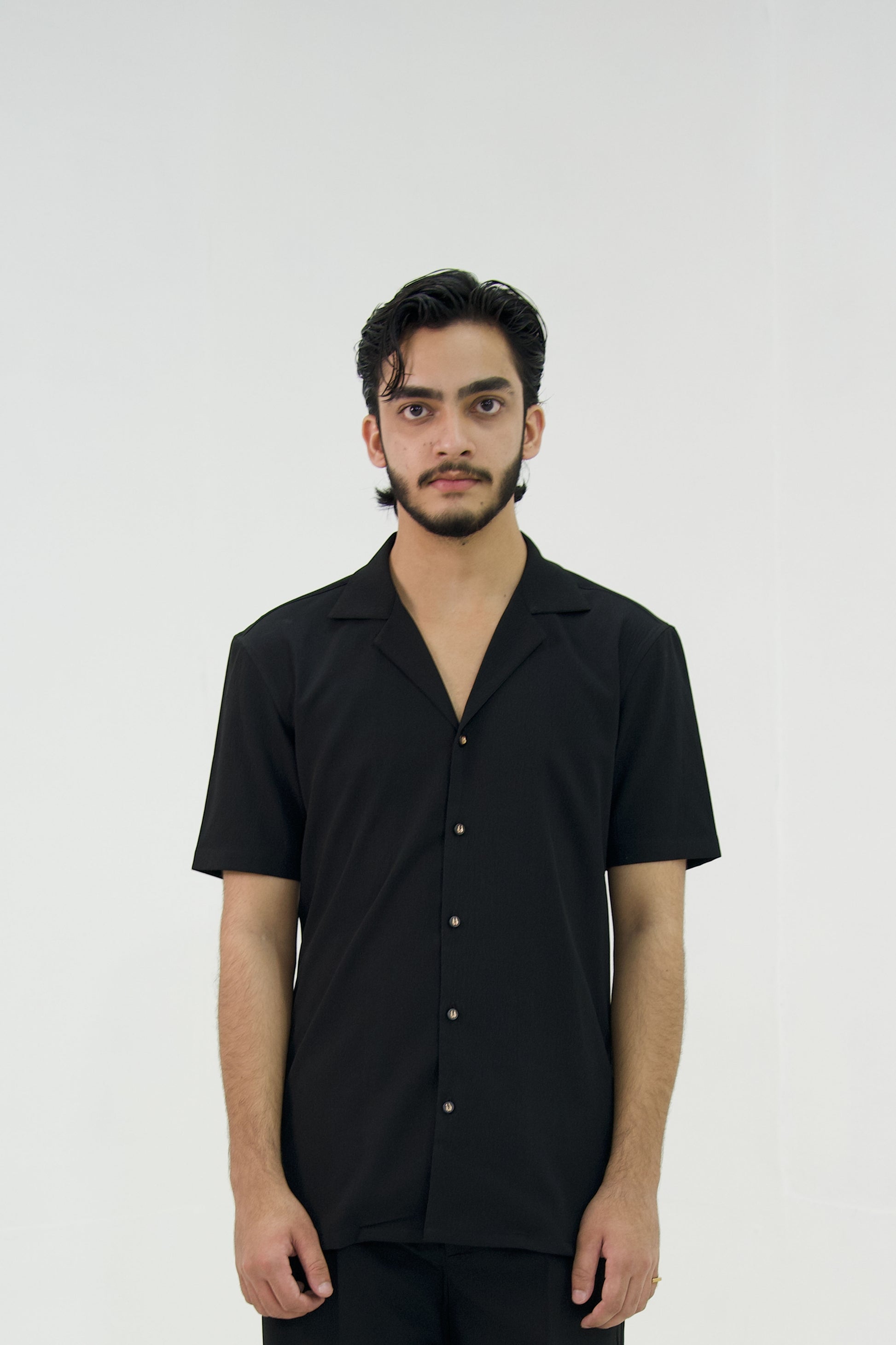 Man posing in a black cuban collar shirt by Abbod Atelier on a white studio background.