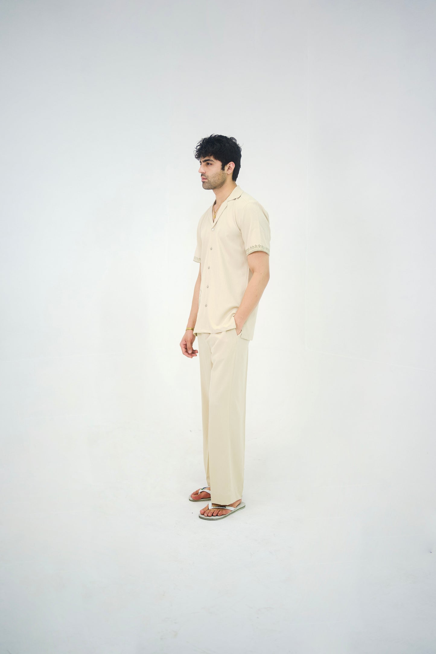 Man posing in a beige cuban collar shirt and matching tailored trousers by Abbod Atelier on a white studio background.