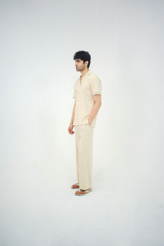Man posing in a beige cuban collar shirt and matching tailored trousers by Abbod Atelier on a white studio background.