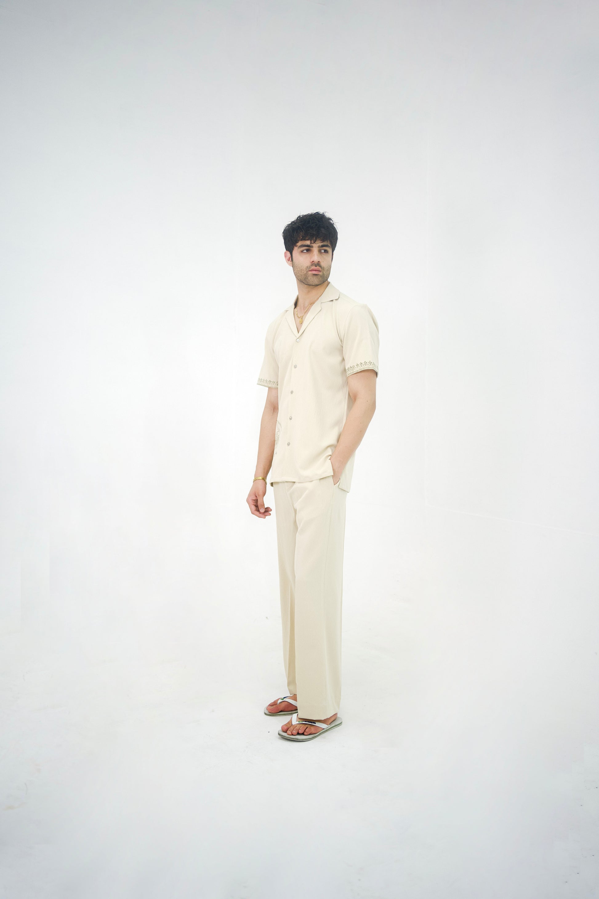 Man posing in a beige cuban collar shirt and matching tailored trousers by Abbod Atelier on a white studio background.