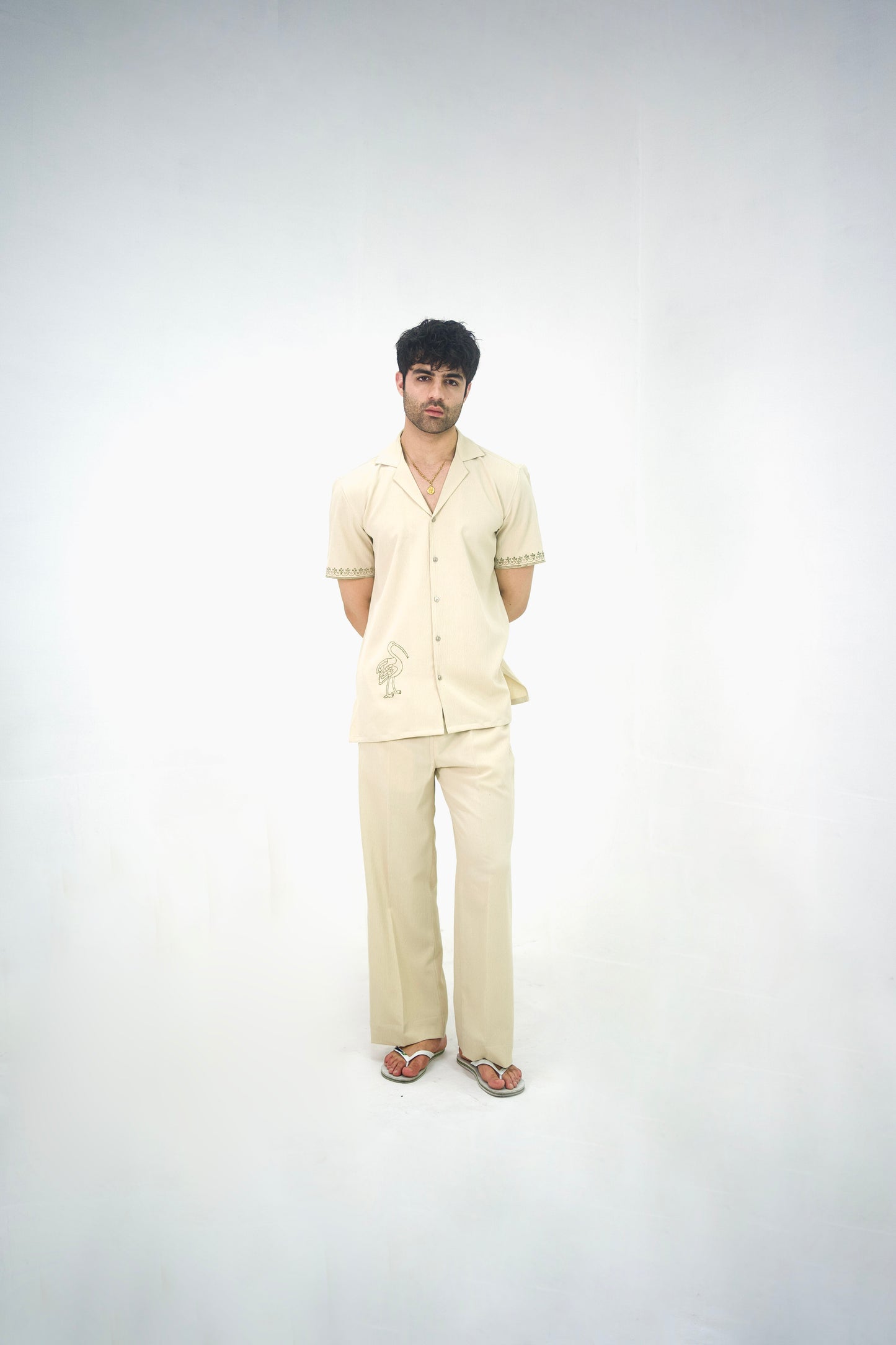 Man posing in a beige cuban collar shirt and matching tailored trousers by Abbod Atelier on a white studio background.