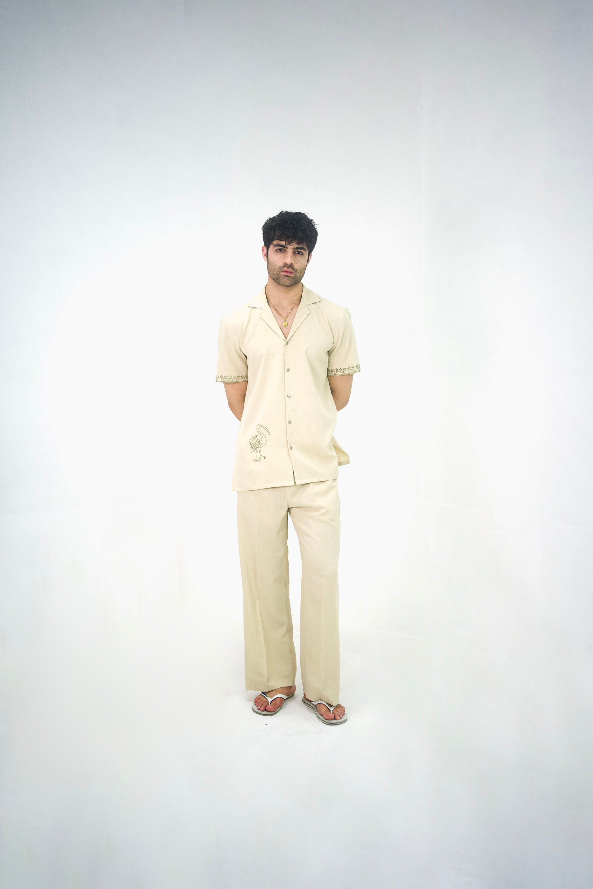 Man posing in a beige cuban collar shirt and matching tailored trousers by Abbod Atelier on a white studio background.