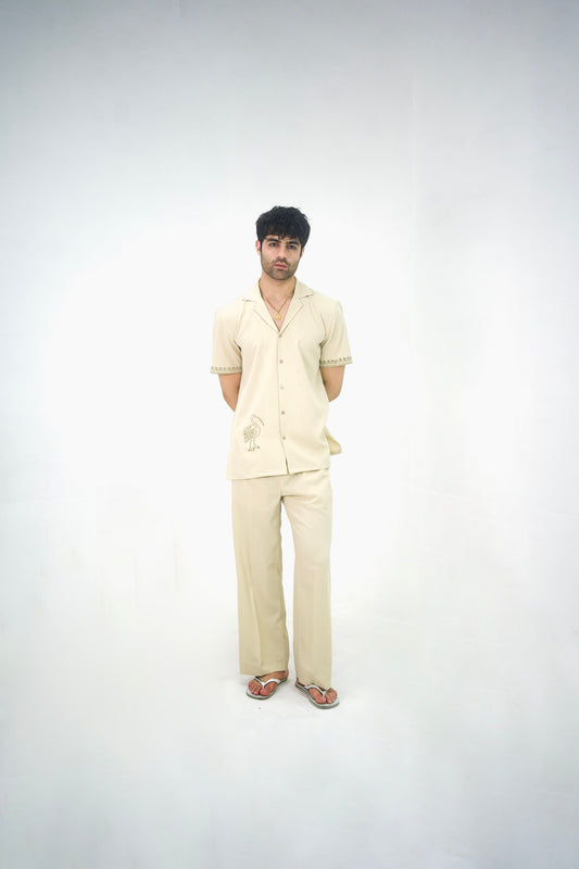 Man posing in a beige cuban collar shirt and matching tailored trousers by Abbod Atelier on a white studio background.