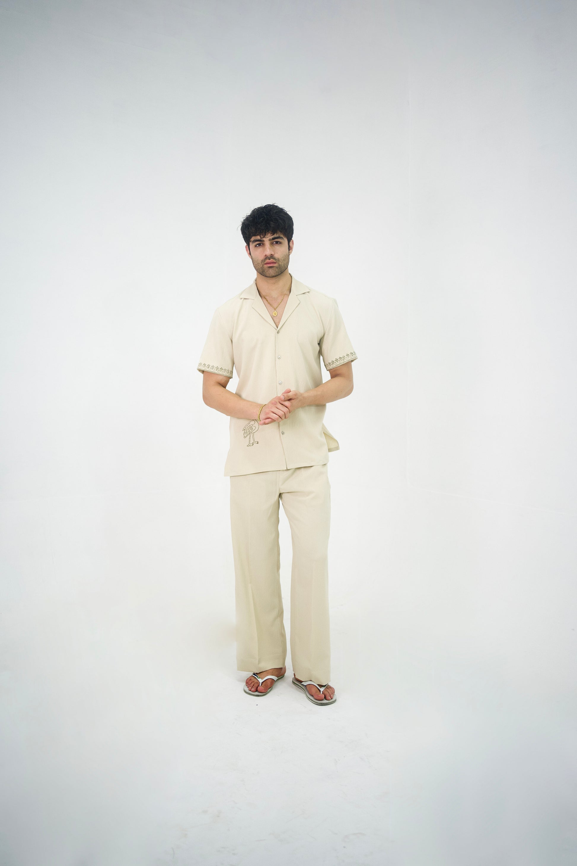 Man posing in a beige cuban collar shirt and matching tailored trousers by Abbod Atelier on a white studio background.