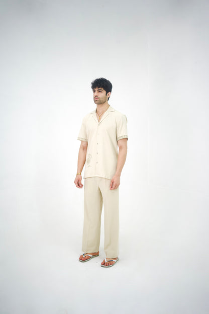 Man posing in a beige cuban collar shirt and matching tailored trousers by Abbod Atelier on a white studio background.