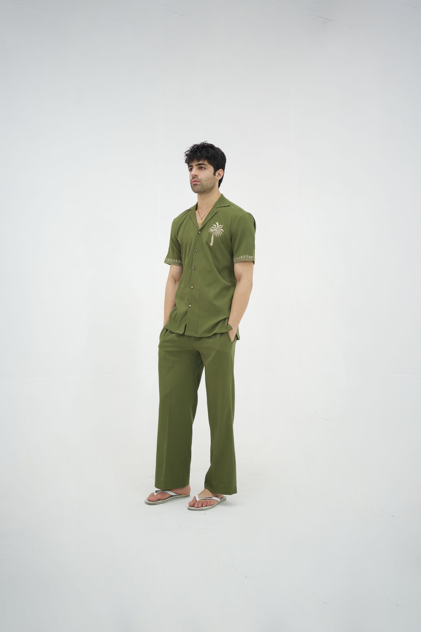 Man posing in a olive green cuban collar shirt and matching tailored trousers by Abbod Atelier on a white studio background.