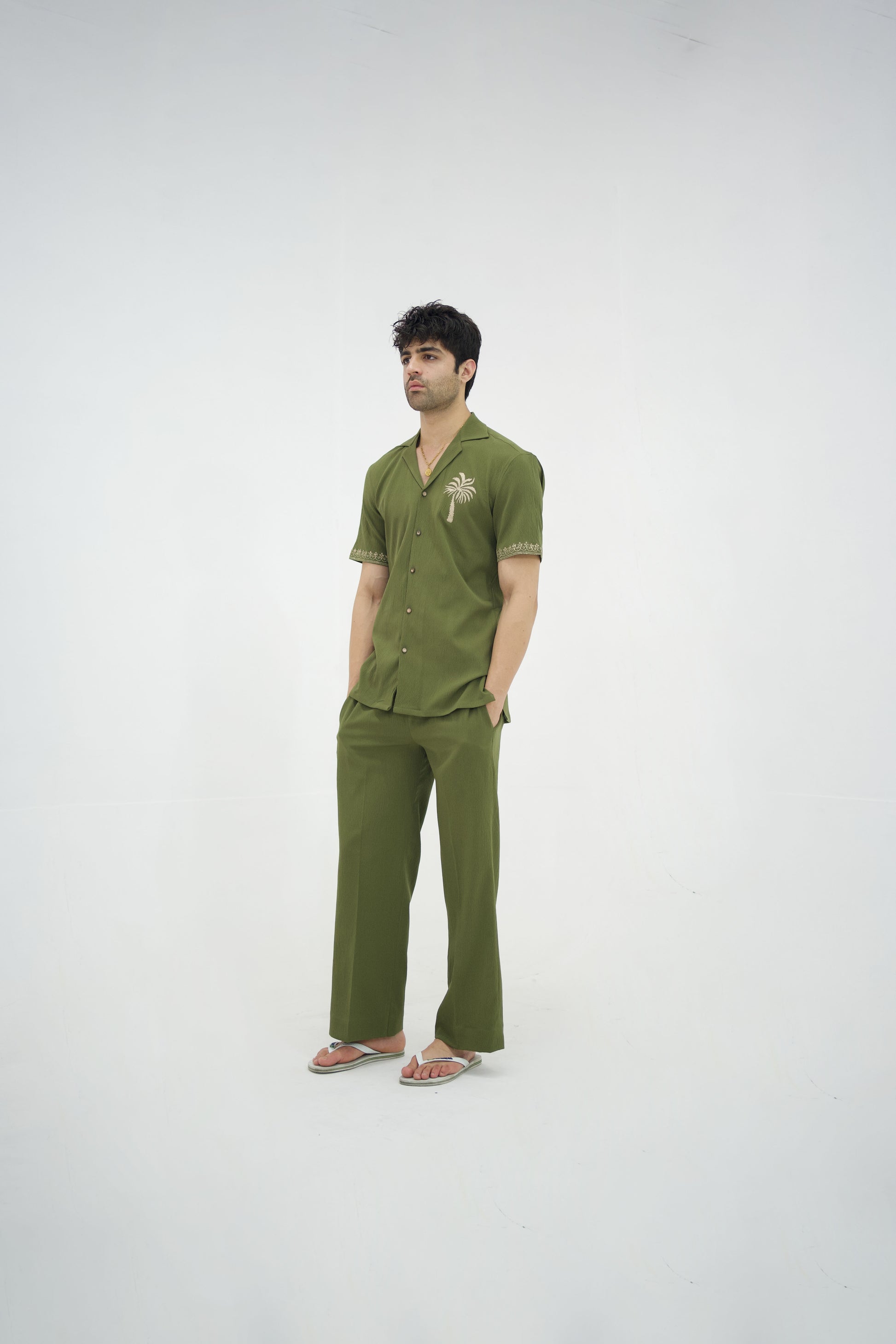 Man posing in a olive green cuban collar shirt and matching tailored trousers by Abbod Atelier on a white studio background.