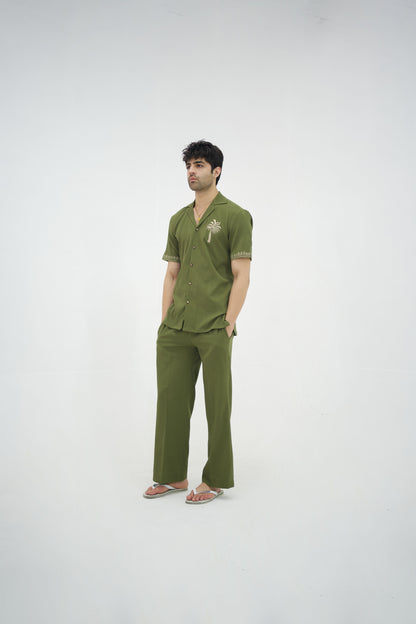 Man posing in a olive green cuban collar shirt and matching tailored trousers by Abbod Atelier on a white studio background.