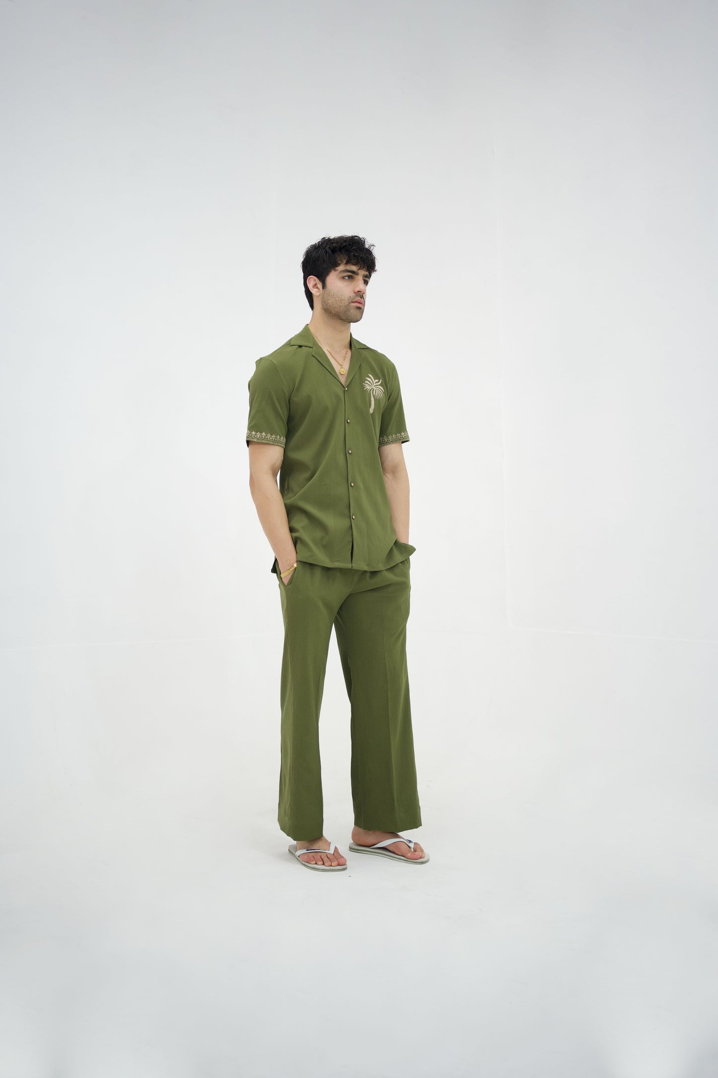 Man posing in a olive green cuban collar shirt and matching tailored trousers by Abbod Atelier on a white studio background.