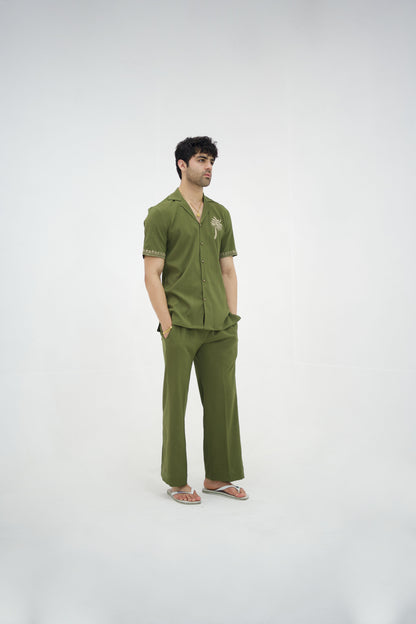 Man posing in a olive green cuban collar shirt and matching tailored trousers by Abbod Atelier on a white studio background.