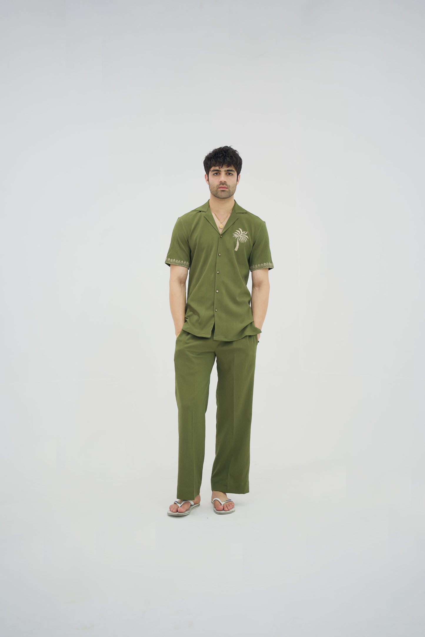 Man posing in a olive green cuban collar shirt and matching tailored trousers by Abbod Atelier on a white studio background.
