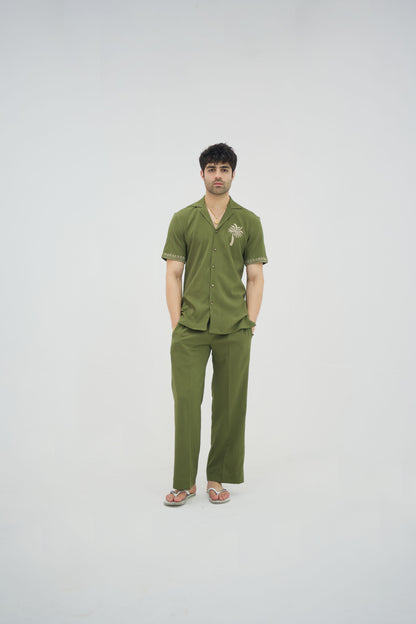 Man posing in a olive green cuban collar shirt and matching tailored trousers by Abbod Atelier on a white studio background.