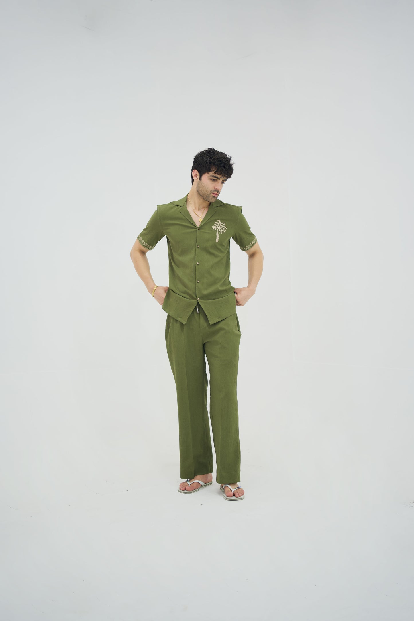 Man posing in a olive green cuban collar shirt and matching tailored trousers by Abbod Atelier on a white studio background.