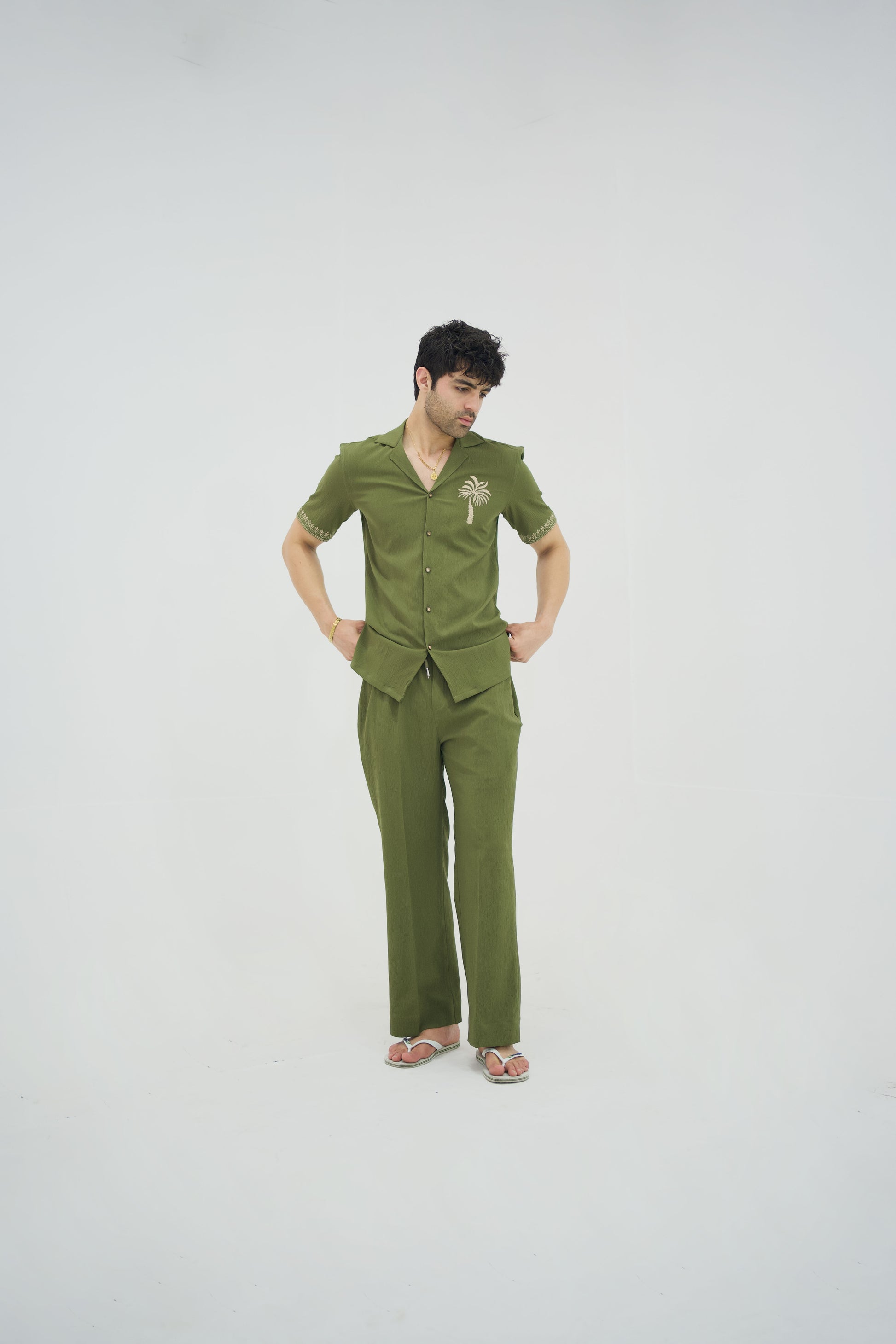 Man posing in a olive green cuban collar shirt and matching tailored trousers by Abbod Atelier on a white studio background.