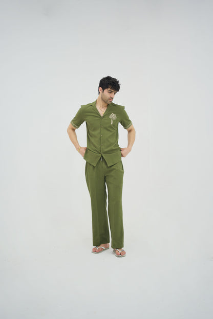 Man posing in a olive green cuban collar shirt and matching tailored trousers by Abbod Atelier on a white studio background.