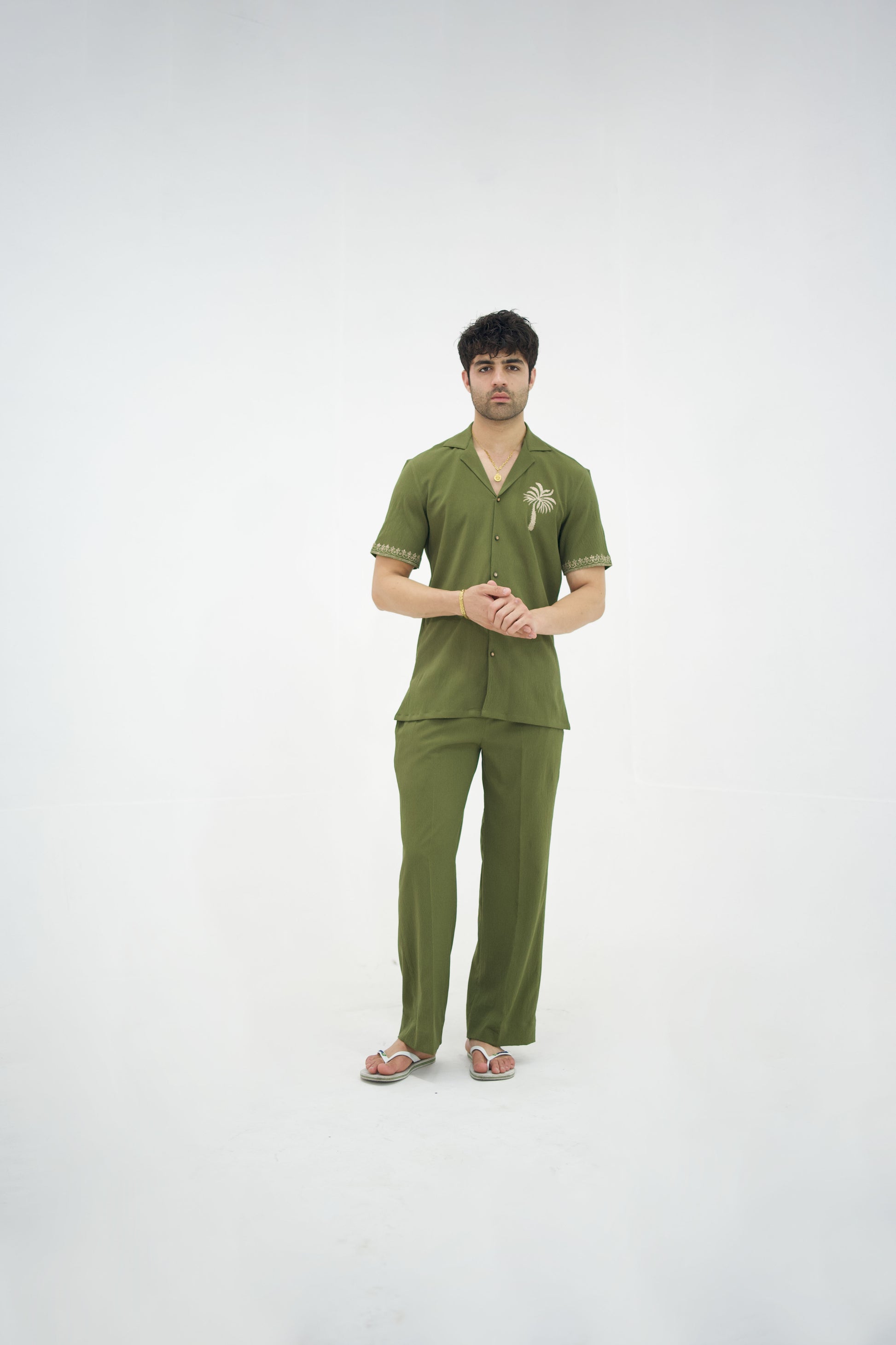 Man posing in a olive green cuban collar shirt and matching tailored trousers by Abbod Atelier on a white studio background.