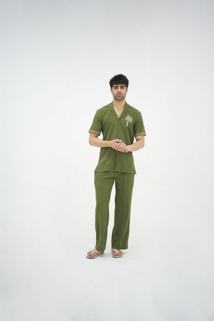 Man posing in a olive green cuban collar shirt and matching tailored trousers by Abbod Atelier on a white studio background.