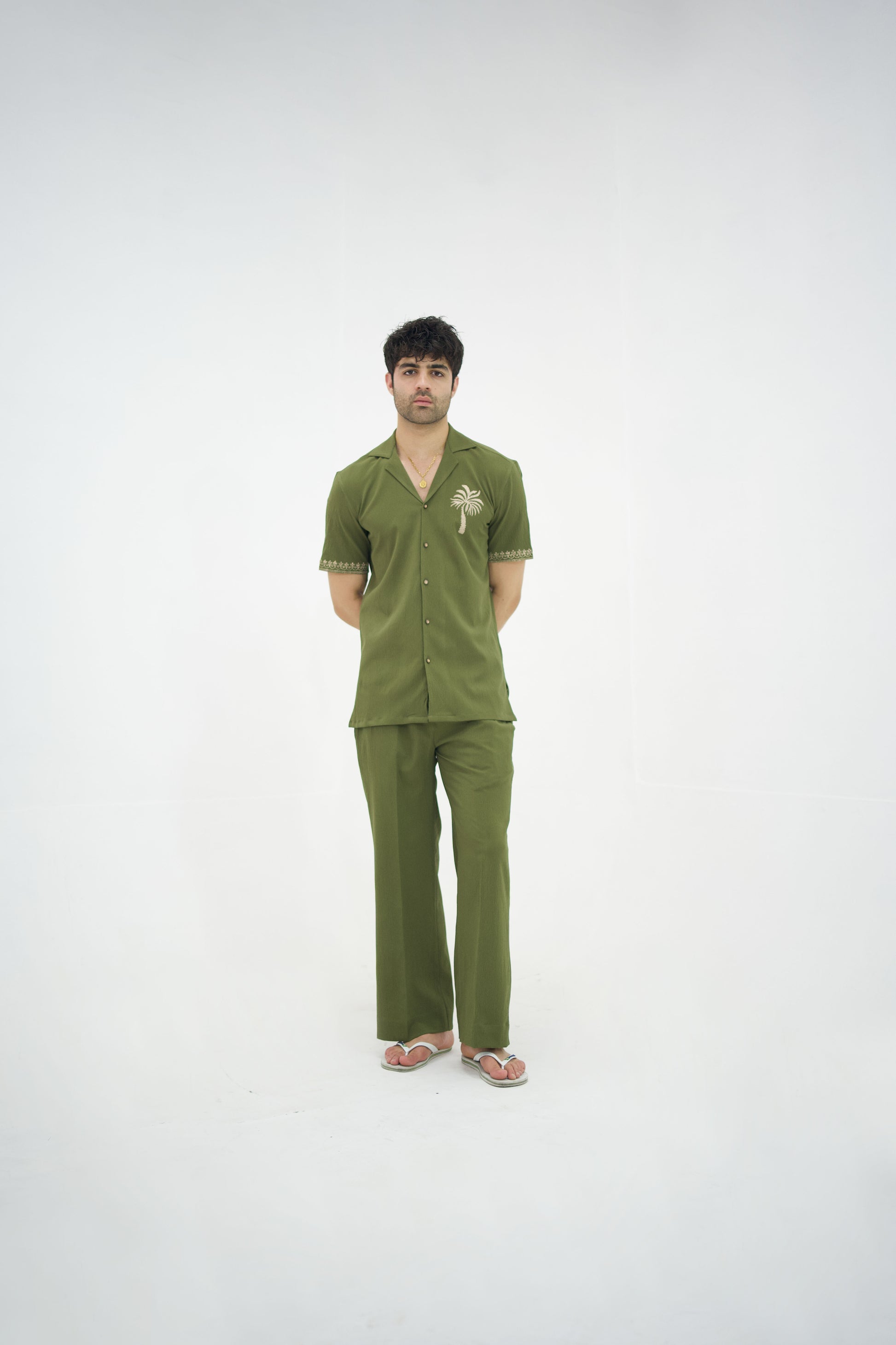 Man posing in a olive green cuban collar shirt and matching tailored trousers by Abbod Atelier on a white studio background.