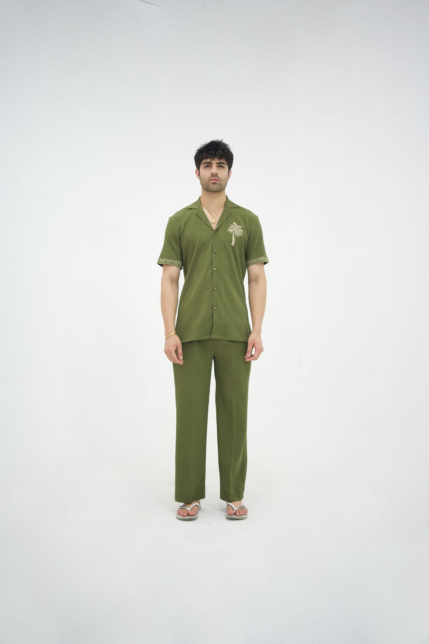 Man posing in a olive green cuban collar shirt and matching tailored trousers by Abbod Atelier on a white studio background.