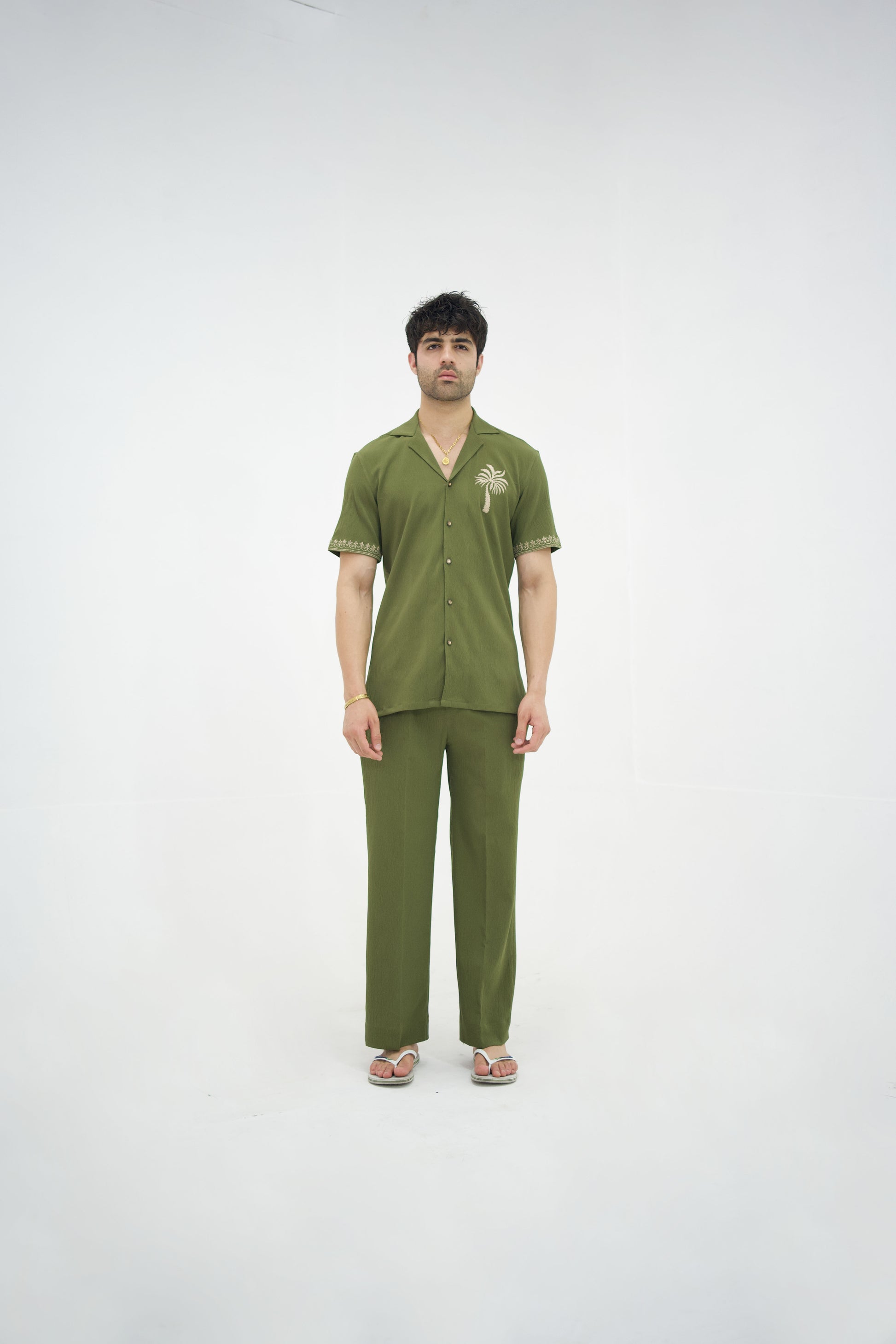 Man posing in a olive green cuban collar shirt and matching tailored trousers by Abbod Atelier on a white studio background.
